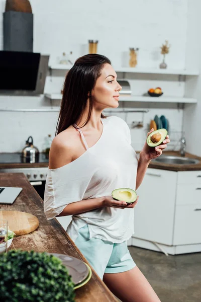 Menina Muito Elegante Segurando Cortar Abacate Perto Mesa Cozinha — Fotografia de Stock