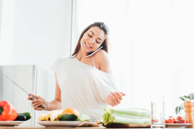 Mutfakta yemek yaparken akıllı telefonda konuşan neşeli genç kadın