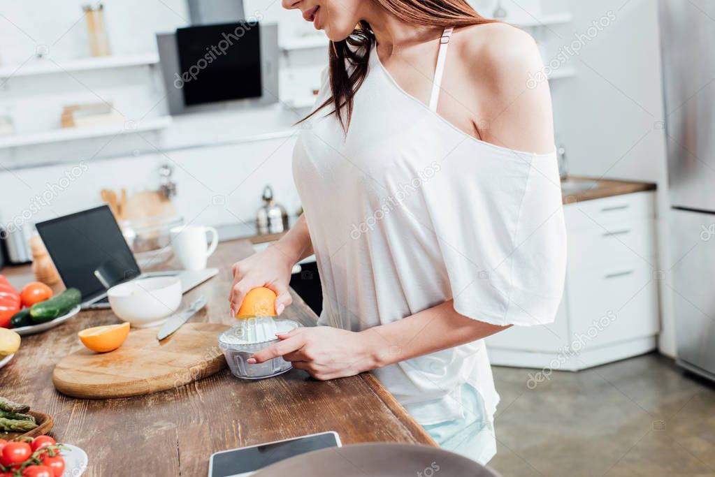 Partial view of woman making fresh orange juice in kitchen