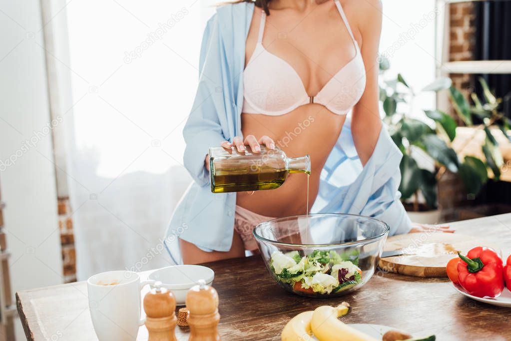 Cropped view of sexy woman in white underwear adding oil at salad