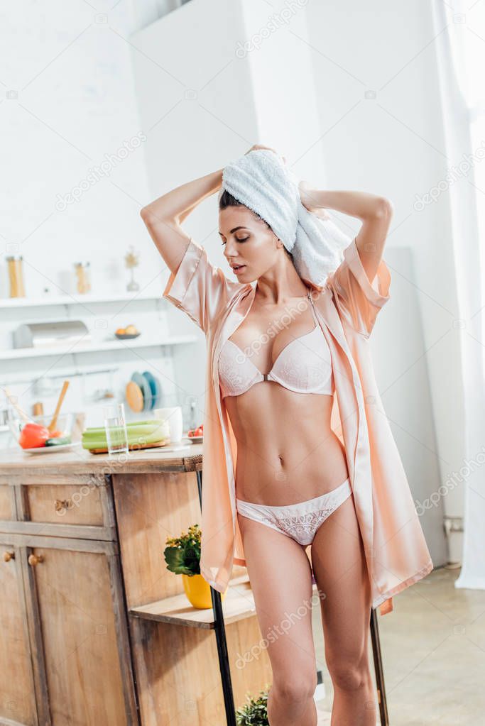 Sexy woman in white lingerie and housecoat with towel on head in kitchen