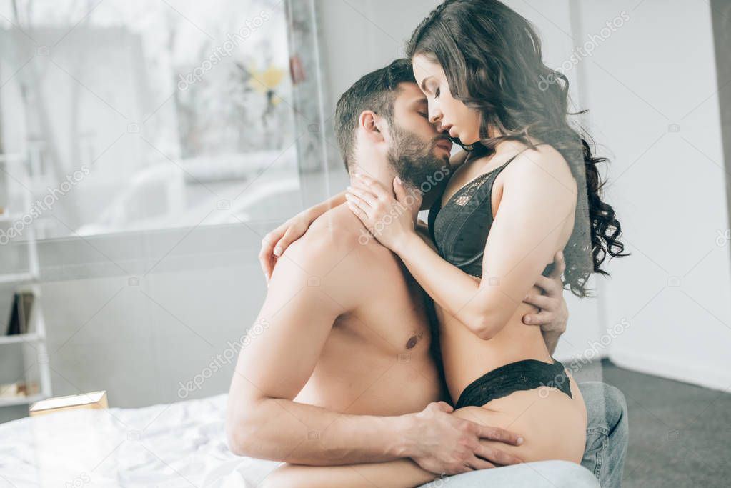 passionate couple kissing while sitting on bed at home