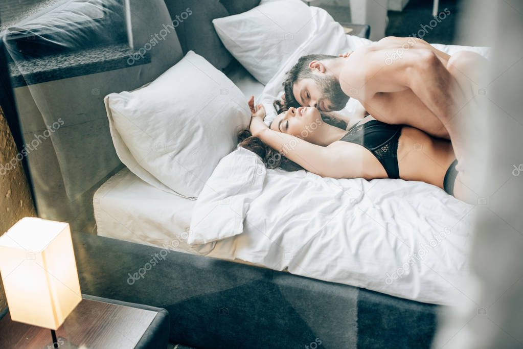 bearded shirtless man kissing passionate brunette woman on bed 