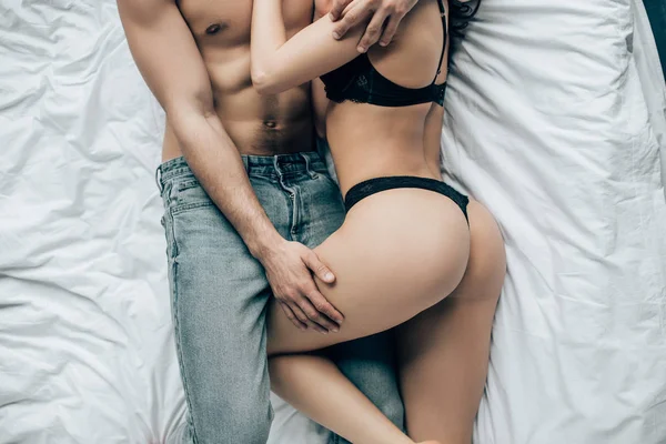 上半身裸の男がベッドの上に横たわっている間黒い下着のセクシーな女性に触れるのトリミング ビュー — ストック写真