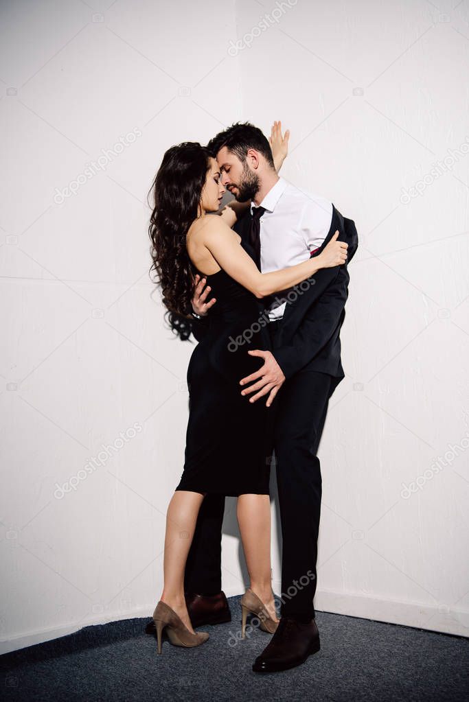 attractive brunette woman undressing handsome man near white wall 