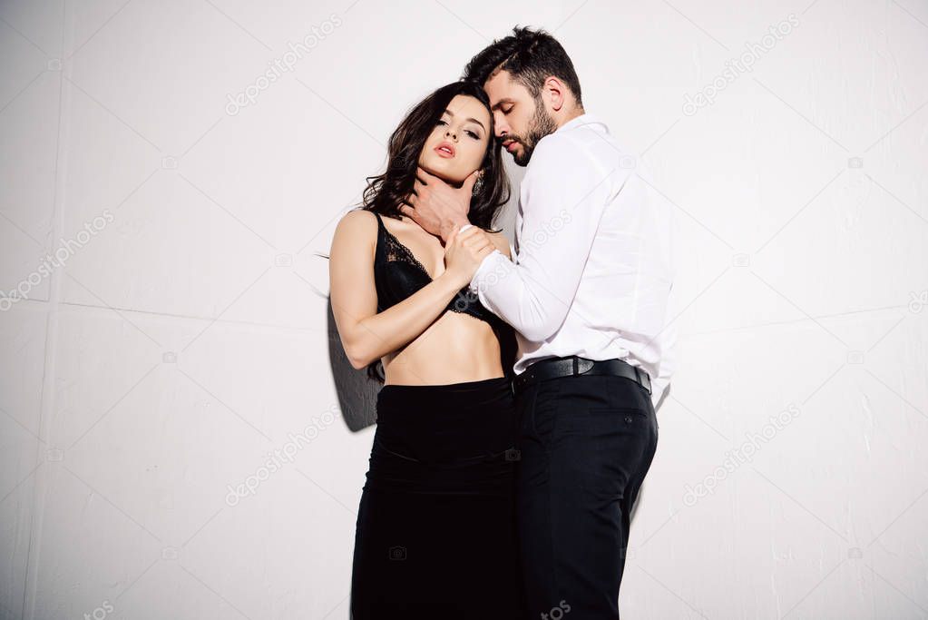 handsome man touching sexy brunette woman in black bra standing on white 