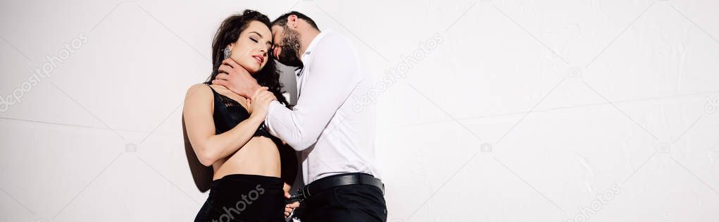 panoramic shot of handsome man touching neck of beautiful woman in black lace bra on white 