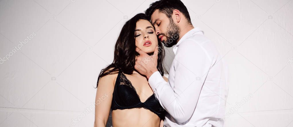 panoramic shot of handsome man touching face of sexy woman in black bra standing on white 