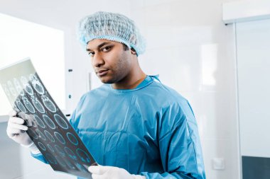iyi görünümlü Doktor tıbbi kap ve üniforma tutarak x-ışını ve kamera bakıyor 