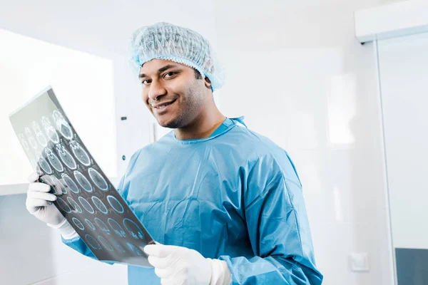 smiling doctor in uniform and medical cap holding x-ray in and looking at camera