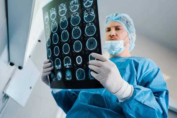 low angle view of doctor in medical cap and uniform holding x-ray in clinic