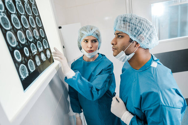 Красивые и красивые врачи в униформе и медицинских масках смотрят на рентген и говорят

