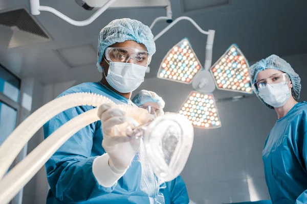 doctor and nurse in uniforms and medical caps holding mask in operating room