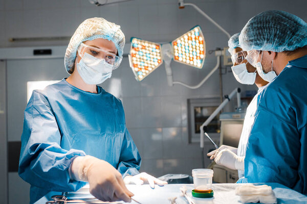 nurse holding equipment and doctors in uniforms and medical caps in operating room