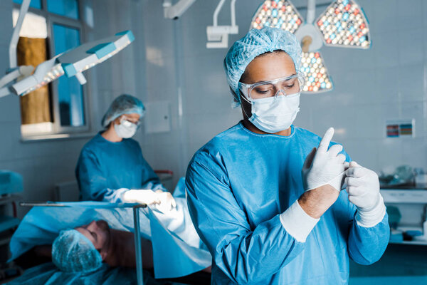 selective focus of doctor in uniform putting off latex gloves in operating room