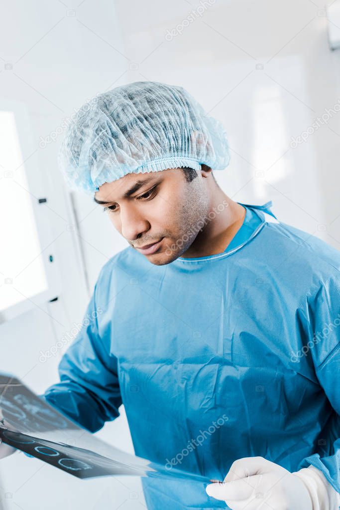 handsome doctor in medical cap and uniform holding x-ray in clinic 