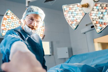 cerrahın seçici odağı, kamera görünümlü ve hastanın elini tutan üniforma ve tıbbi maske 