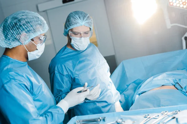 nurse in uniform and medical mask giving medical equipment to surgeon