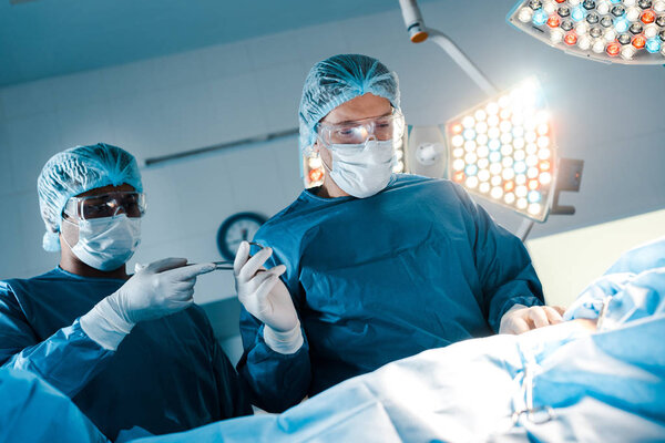 nurse in uniform and medical mask giving medical equipment to surgeon 