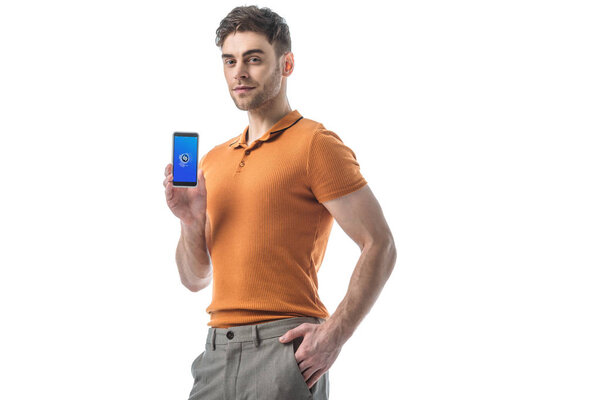 smiling man with hand in pocket holding smartphone with shazam app on screen isolated on white