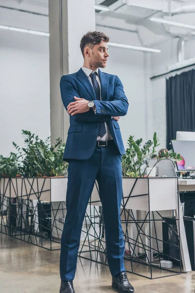 ハンサムな 自信に満ちたビジネスマンは 腕を組んでオフィスに立ち 目をそらす — ストック写真