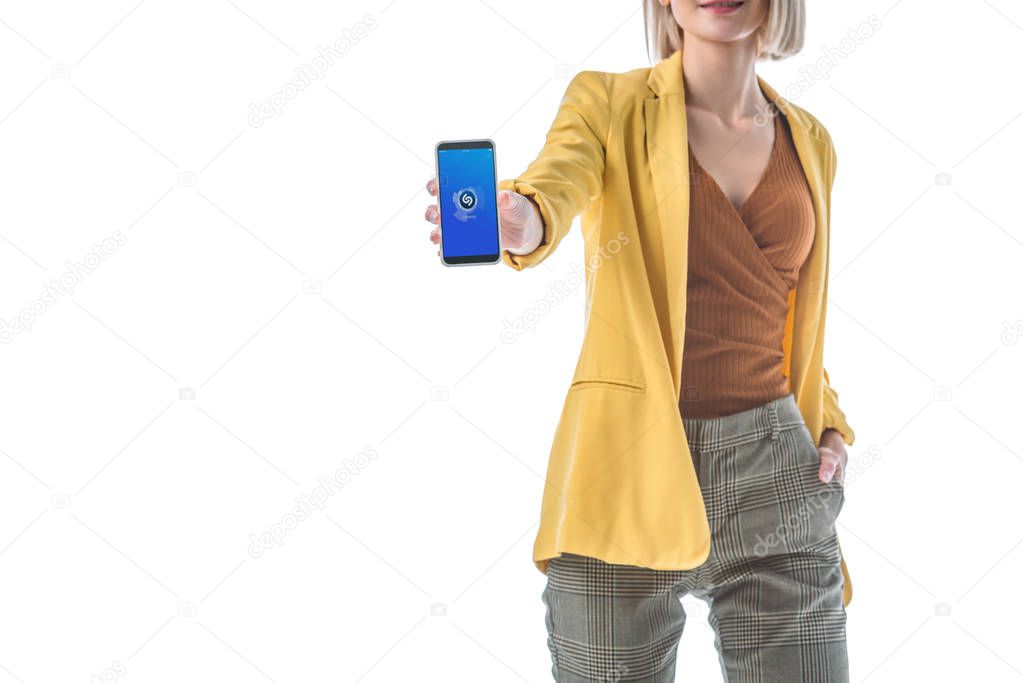 partial view of trendy woman holding smartphone with shazam app on screen isolated on white