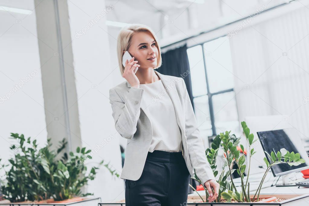 attractive blonde businesswoman in formal wear talking on smartphone in office