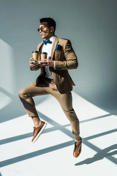 Stylish Mixed Race Man Suit Holding Coffee Jumping Grey Sunlight — Stock Photo, Image