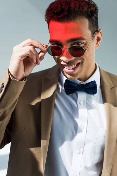 时尚的混血男子在西装和太阳镜看相机在灰色与红灯 — 图库照片