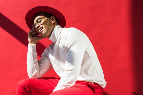 Elegante Hombre Raza Mixta Sombrero Gafas Sentado Sonriendo Posando Rojo — Foto de Stock
