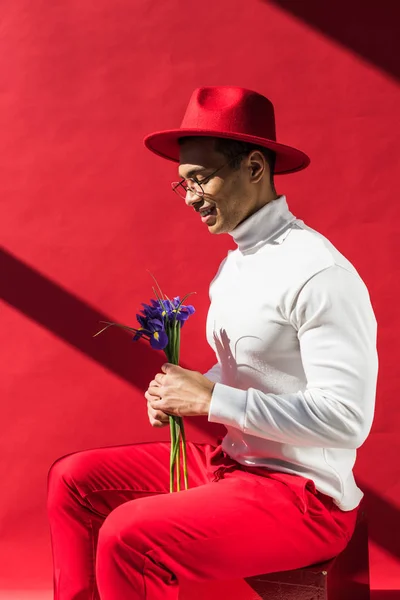 帽子とメガネで花を抱き 赤で微笑むスタイリッシュなミックスレースマン — ストック写真