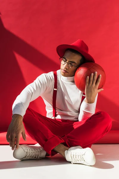 帽子とサスペンダーの座って 赤でバスケットボールのポーズでファッショナブルな混合レース男 — ストック写真