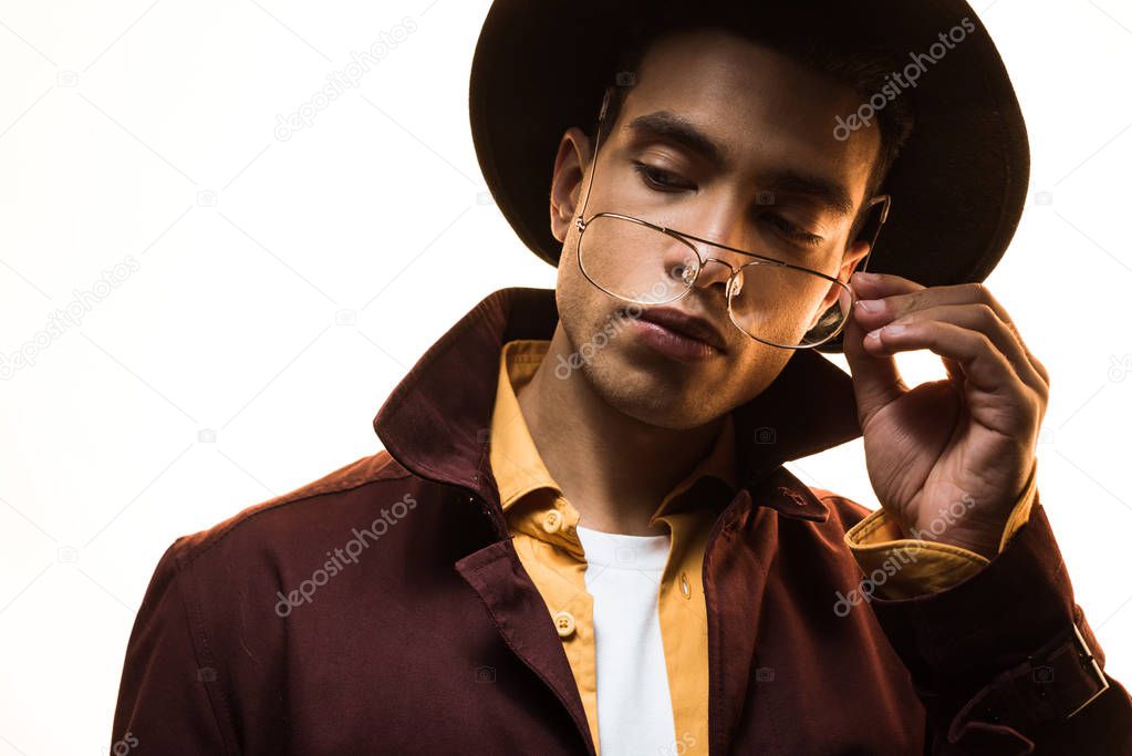 stylish mixed race man in hat adjusting glasses and posing isolated on white