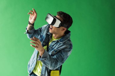 surprised mixed race man in vr headset gesturing while experiencing virtual reality on green screen clipart