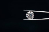 transparent pure shiny diamond in tweezers isolated on black