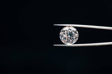 transparent pure shiny diamond in tweezers isolated on black clipart