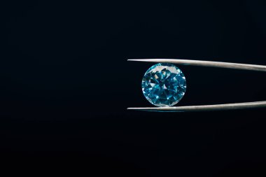 colorful blue sparkling diamond in tweezers isolated on black clipart