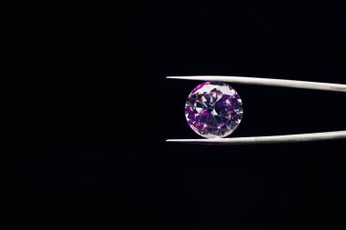 colorful purple sparkling diamond in tweezers isolated on black clipart