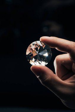 cropped view of man holding big clear shiny diamond on black background clipart