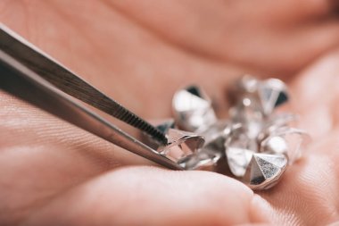 close up of tweezers near shiny diamonds in hand clipart