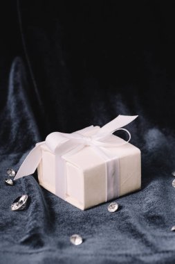 gift box with satin white ribbon and bow near pure diamonds on blue cloth clipart