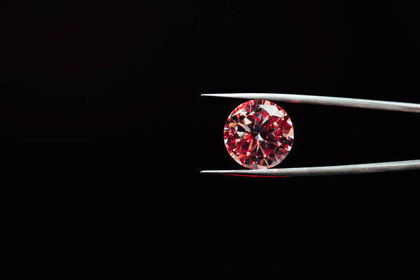colorful red sparkling diamond in tweezers isolated on black