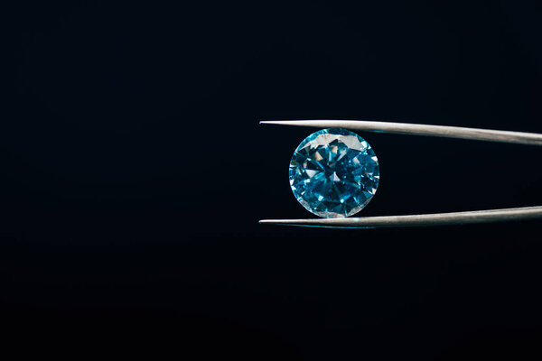 colorful blue sparkling diamond in tweezers isolated on black