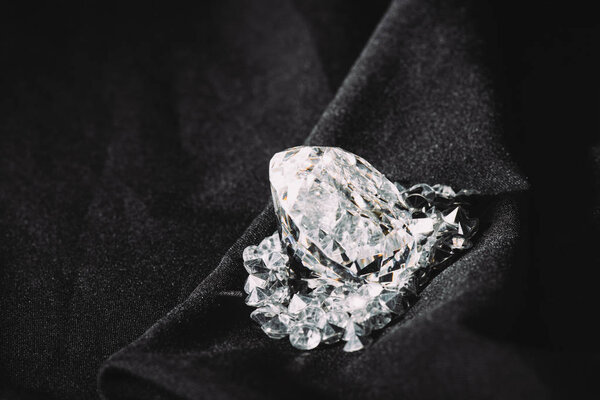 sparkling big diamond among small on black textured shiny cloth 