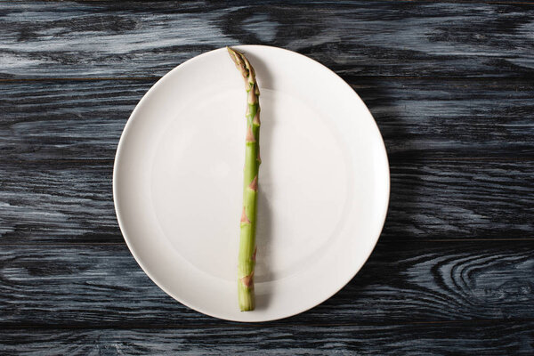 top view of raw asparagus on plate on grey wooden background
