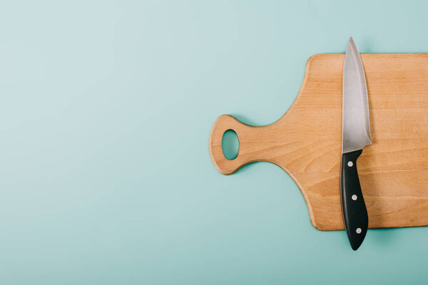 top view of wooden cutting board with knife on blue background with copy space