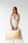 krásná dívka drží kufr stoje na bílém 