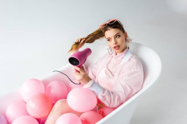 beyaz üzerine pembe hava Balonlu küvet içinde yatan fön kullanan çekici kız 