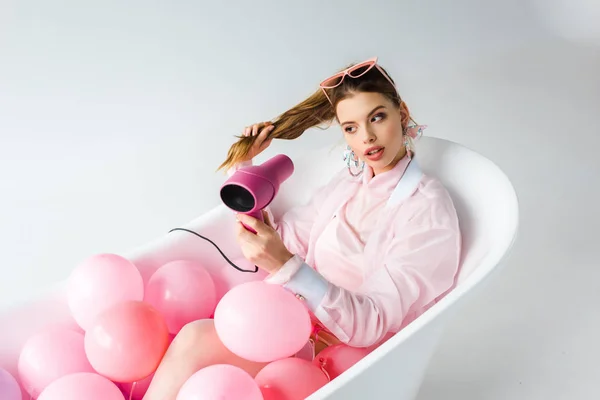 Menina Atraente Usando Secador Cabelo Enquanto Deitado Banheira Com Balões — Fotografia de Stock