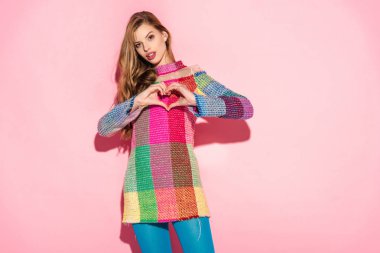Pembe üzerinde kalp şeklinde işaret gösteren ekose elbiseli çekici kız 
